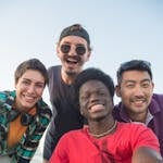 Diverse group of friends smiling and posing together outdoors under a clear sky.